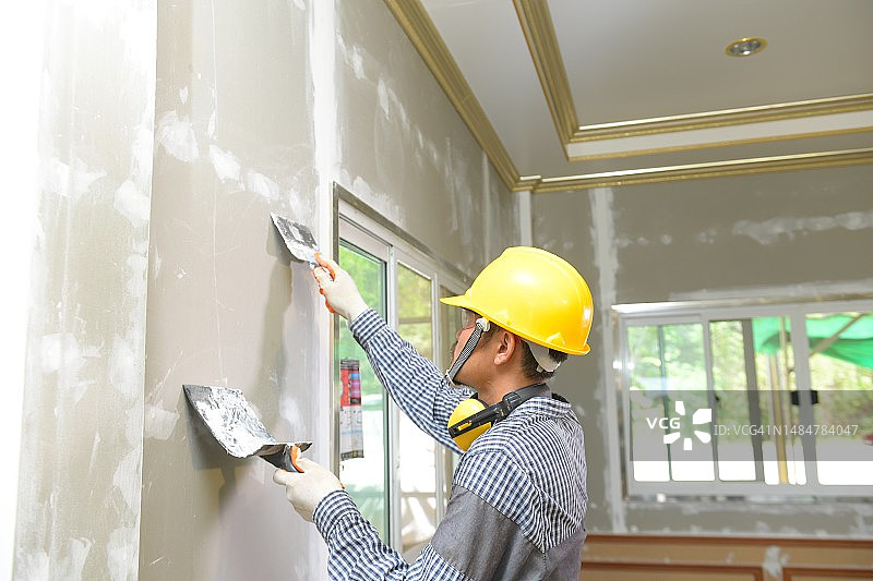 在新建筑房屋内粉刷墙壁的手工工人图片素材