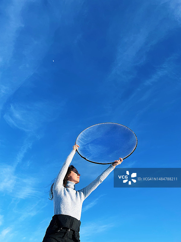 蓝天下手持圆形反光板的女人图片素材
