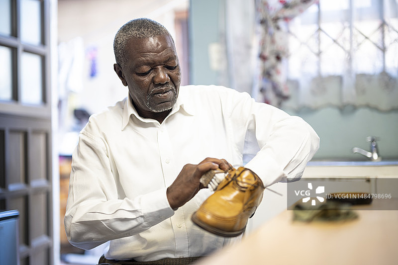 年长的男人在厨房的桌子上用刷子擦亮皮鞋图片素材