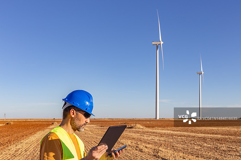 风力工程师在数字平板电脑和智能手机上检查风力涡轮机运行情况的半身像图片素材