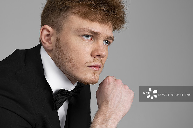 身穿黑色正式西装的自信时尚年轻男人看着镜头，白色背景图片素材