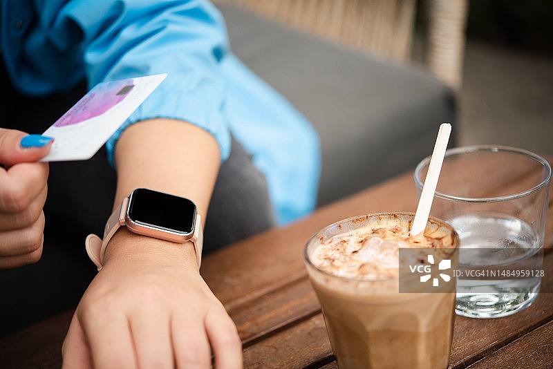 难以辨认的女孩在咖啡馆用信用卡和她的智能手表付款图片素材
