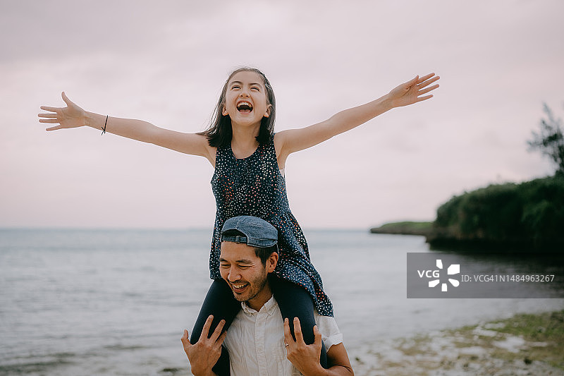 黄昏时分，父亲在海滩上让女儿骑在肩膀上图片素材