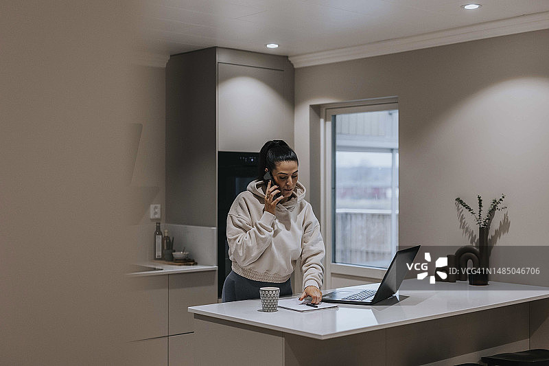 在厨房通过手机交谈的女人图片素材