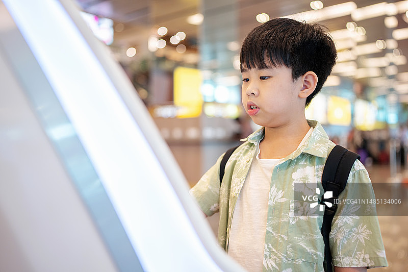 科技让旅行更轻松安全：亚洲男孩在自助值机机办理登机牌，在机场插入护照确认个人信息，周末与家人旅行图片素材