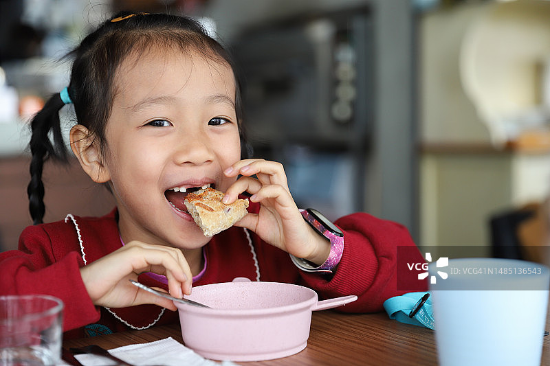 亚洲女孩在餐厅里用儿童餐具吃披萨图片素材