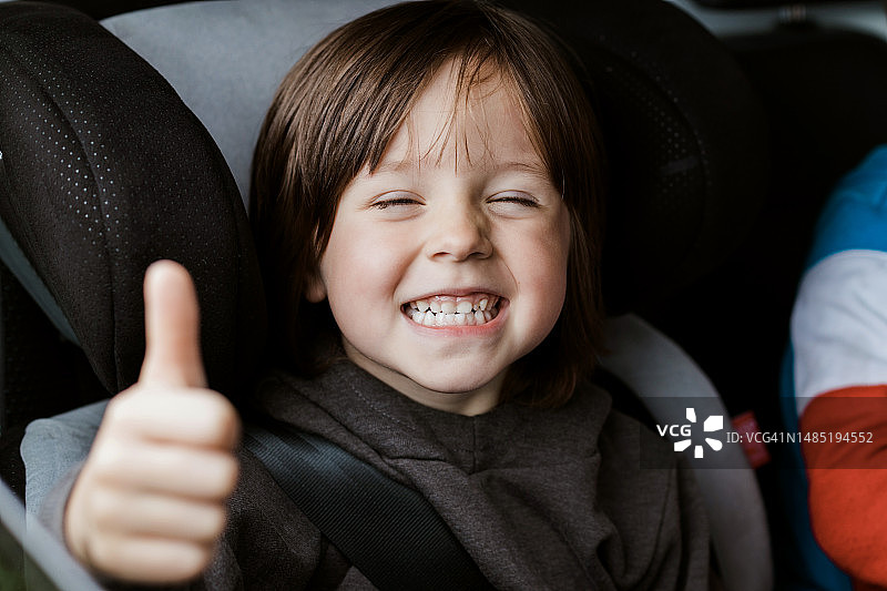 快乐微笑的宝宝坐在汽车座椅上，竖起大拇指图片素材