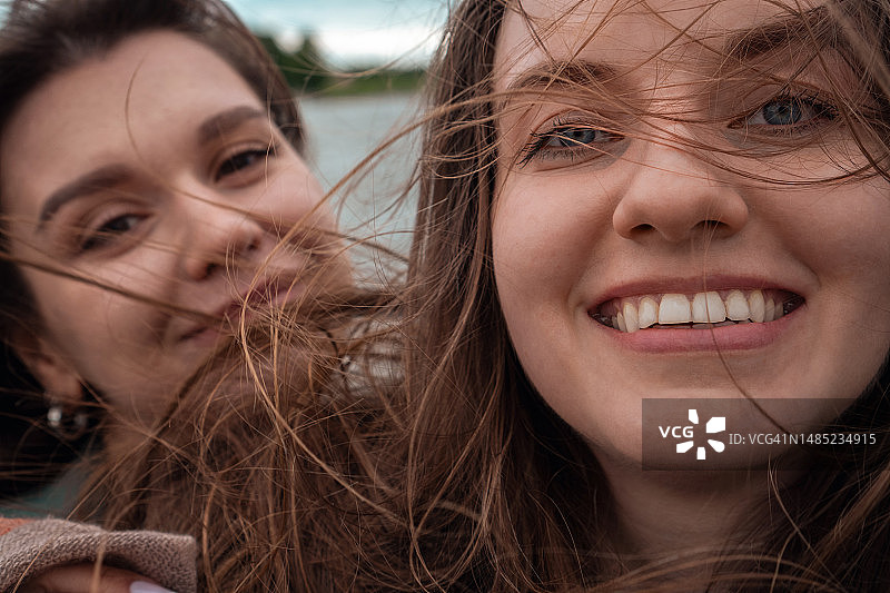 两个快乐的微笑女人在刮风天自拍，两个女性的特写图片素材