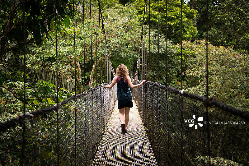 徒步旅行——在哥斯达黎加阿雷纳尔国家公园拉福图纳雨林中的悬索桥上的女人图片素材