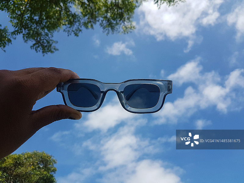 蓝色天空背景上手持太阳镜的手部裁剪图图片素材