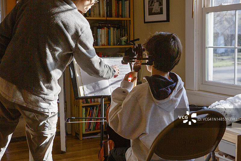 父亲在窗边帮儿子练习大提琴图片素材