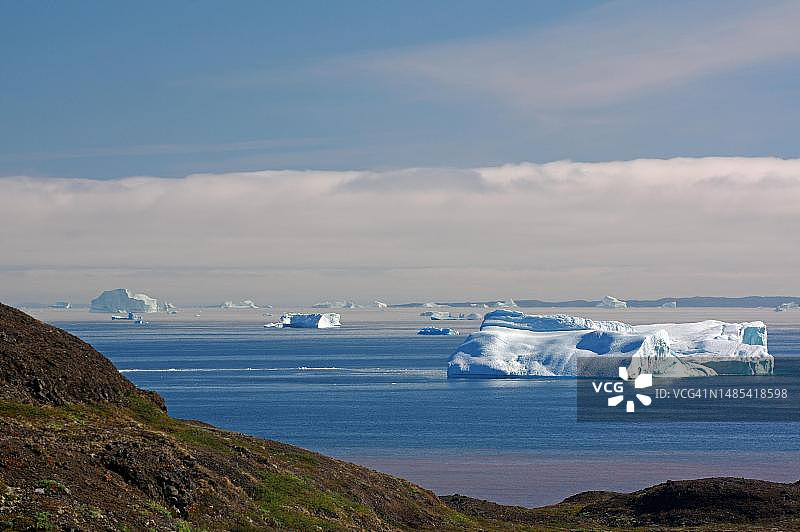 格陵兰岛迪斯科岛，海湾海滩区域被河流染成红色的宽阔海湾中的冰山图片素材