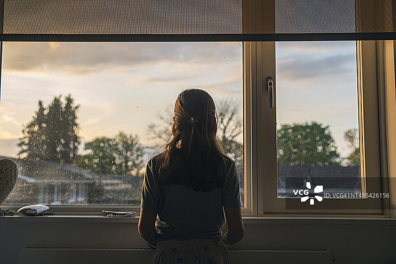 年轻女孩在黄昏时望向窗外的 мощный 肖像图片素材