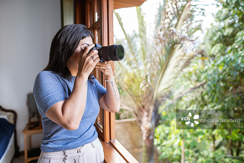 年轻女摄影师在家中从窗户拍照图片素材