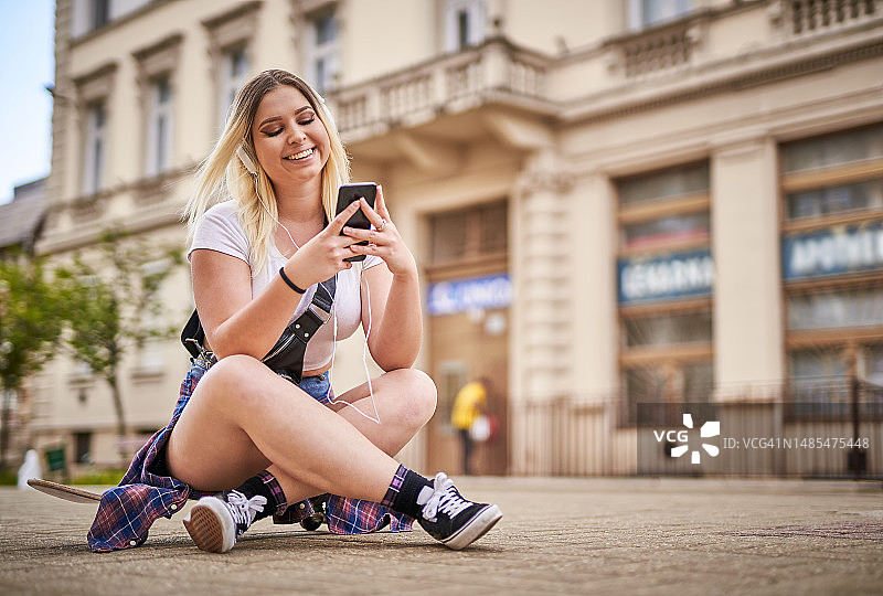 戴着耳机坐在滑板上的快乐年轻女子图片素材
