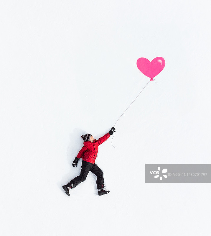 冬季男孩身穿冬装，手持粉色气球的航拍照片图片素材