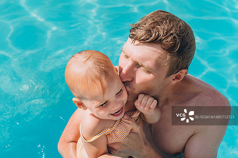 在露天泳池亲吻女儿脸颊的男人图片素材