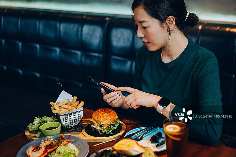 在餐厅用餐时使用智能手机的年轻亚洲女性图片素材