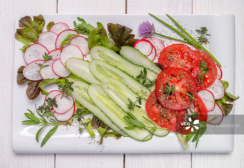 白色盘子上放着西红柿、黄瓜、萝卜的春季纯素沙拉顶视图图片素材