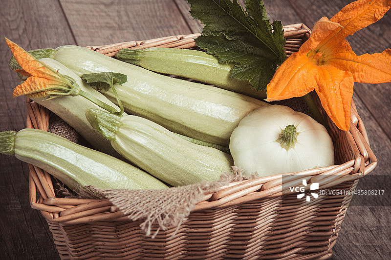 柳条筐装的西葫芦和鲜花，木质背景图片素材