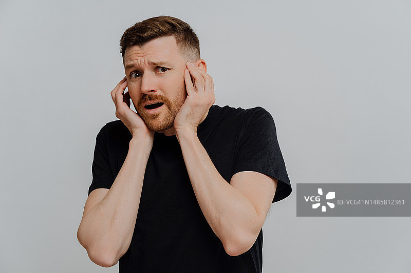 害怕的年轻欧洲男人双手捂脸，害怕可怕的场景，穿着休闲装，俄罗斯图片素材