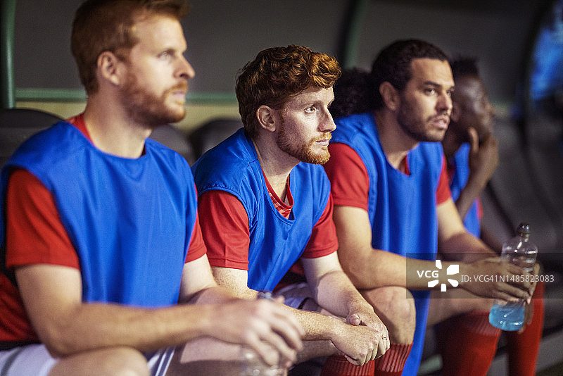 国际足球运动员在替补席观看队友参加关键足球比赛图片素材