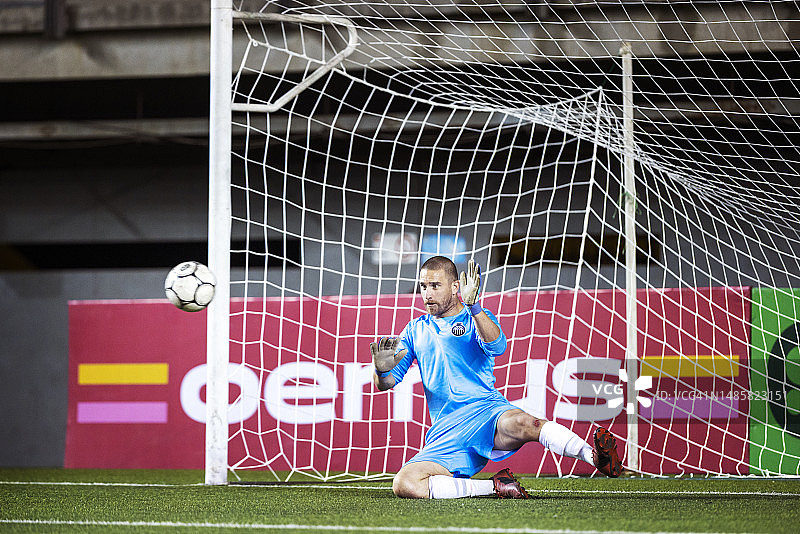 激烈的国际比赛中，敏捷的男子足球守门员猛扑以阻挡射向球门的球图片素材