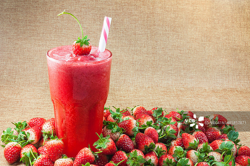 玻璃杯装草莓汁冰沙与传统麻布背景上的新鲜草莓，夏季健康饮品图片素材