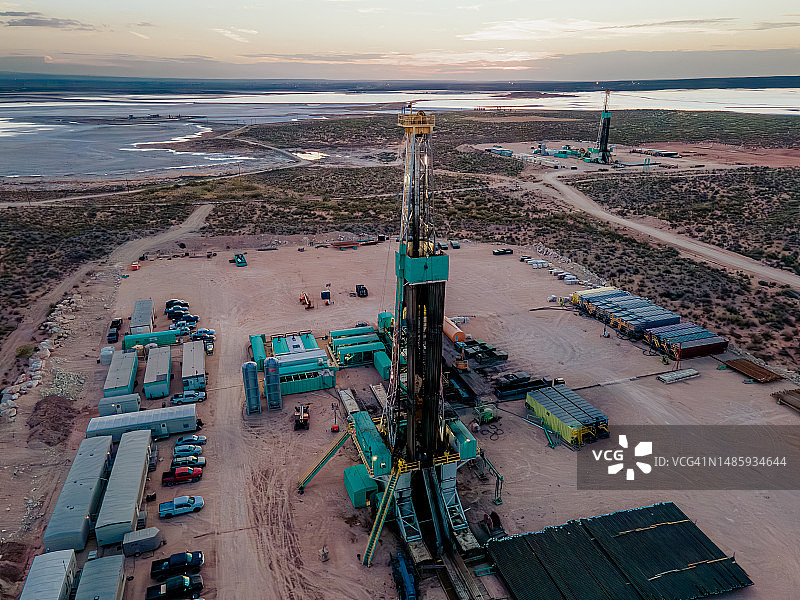 无人机拍摄二叠纪盆地上空壮丽的日落，展示了在广阔的景观中钻探和压裂石油的石油钻井平台图片素材