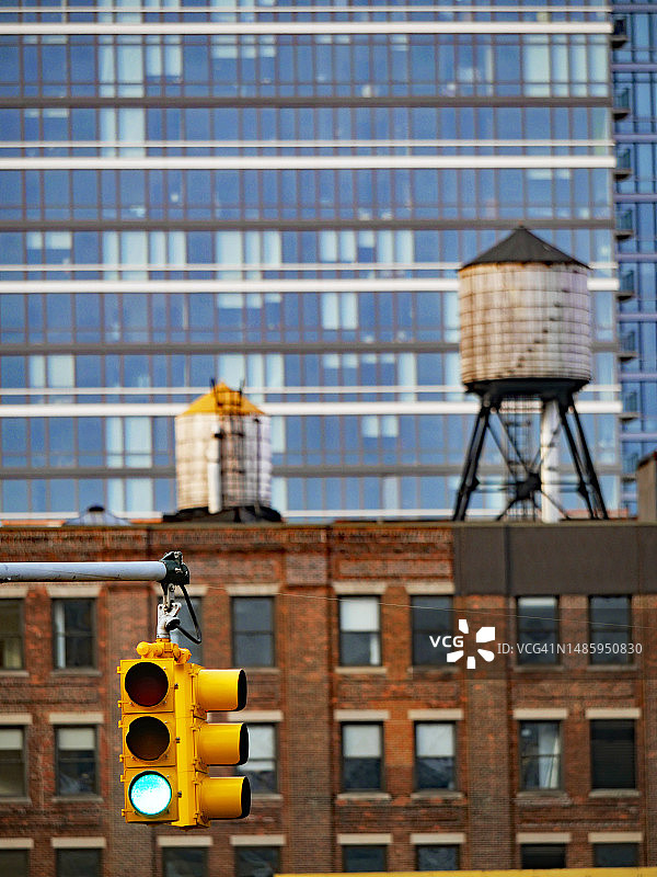 曼哈顿的交通信号灯亮着绿灯，在模糊的背景中，是两座建筑的砖和玻璃外墙，以及一个旧水箱，美国纽约图片素材