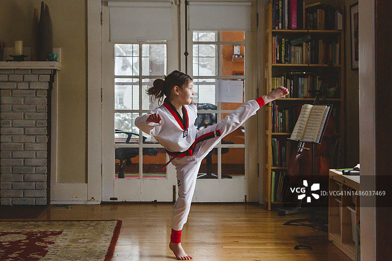 一位年轻女孩在家中穿着跆拳道服踢腿图片素材