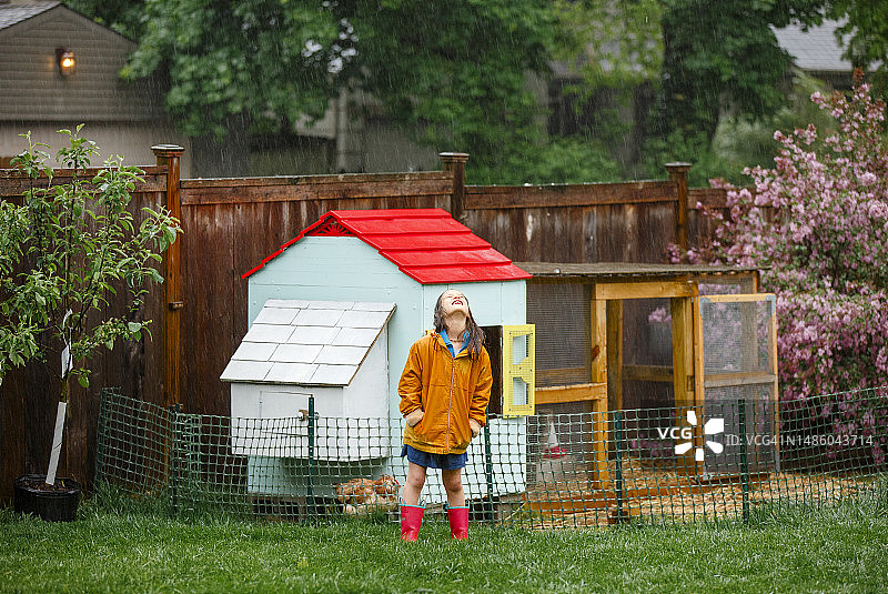 快乐的女孩站在雨中，脸朝上对着鸡舍图片素材