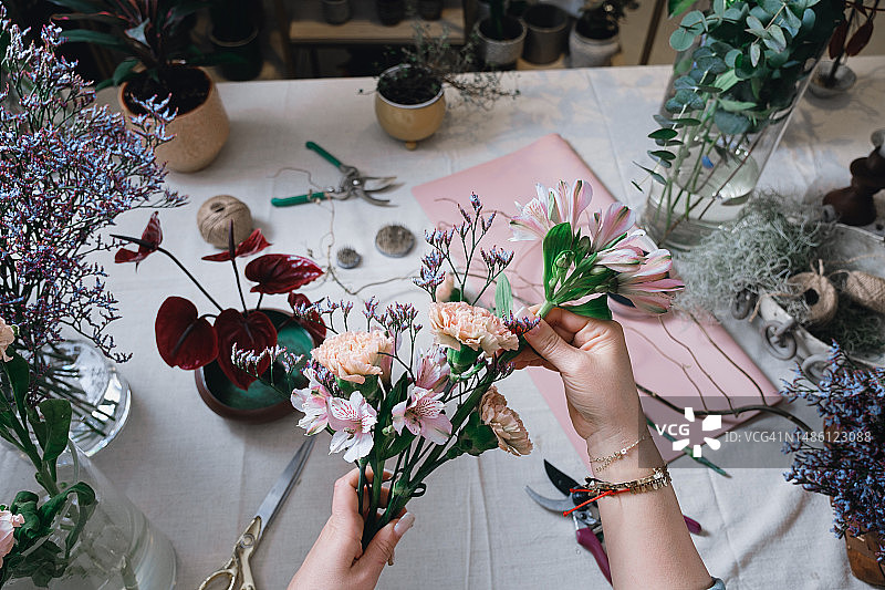 年轻女花艺师在温馨花店打理鲜花，制作精美现代花束。花艺，小本生意，零售概念，花店店员创作创意花束。图片素材