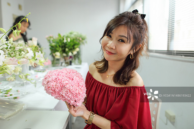 一位美丽的亚洲花艺师拿着心形康乃馨花束庆祝母亲节。图片素材