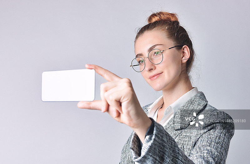 年轻有魅力的女商人穿着正装站立，手持空白手机图片素材