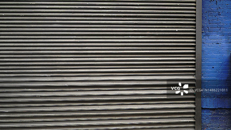 美国纽约曼哈顿的灰色卷帘车库门和蓝色砖墙侧面图图片素材