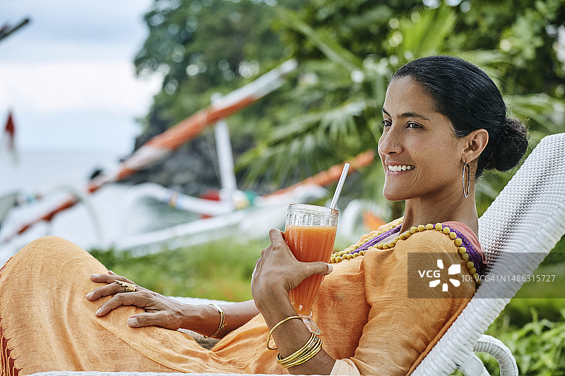 拉丁裔女人坐在躺椅上喝木瓜汁看海图片素材
