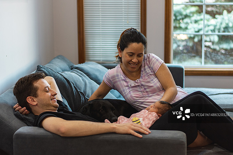 父母在家中与新生女儿和狗互动图片素材