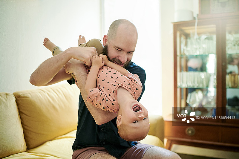 爱，父亲和孩子倒立，在家玩耍和联谊，快乐和幸福。家庭，男性父母和快乐的父亲与孩子在客厅里欢笑、翻转和相爱图片素材
