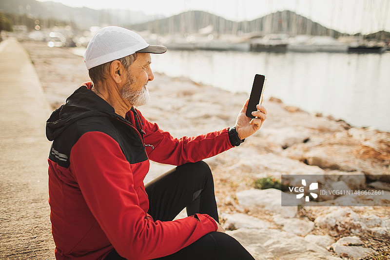 跑步后使用手机进行视频通话的年长男人。关于老年健康积极生活的博主直播图片素材