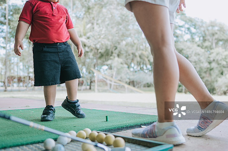 中国男孩在教练的指导下于高尔夫球练习场热身图片素材