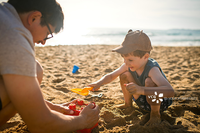 小男孩和他的父亲在夏季的沙滩上建造沙堡图片素材