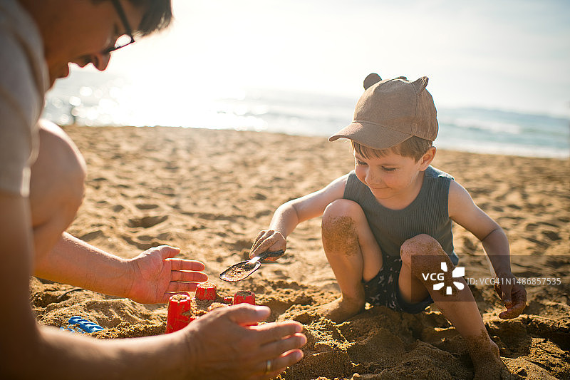 小男孩和他的父亲在夏季的沙滩上建造沙堡图片素材