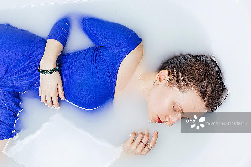 身穿蓝色连衣裙的白人女性在浴缸中沐浴（俯视，选择性聚焦）图片素材