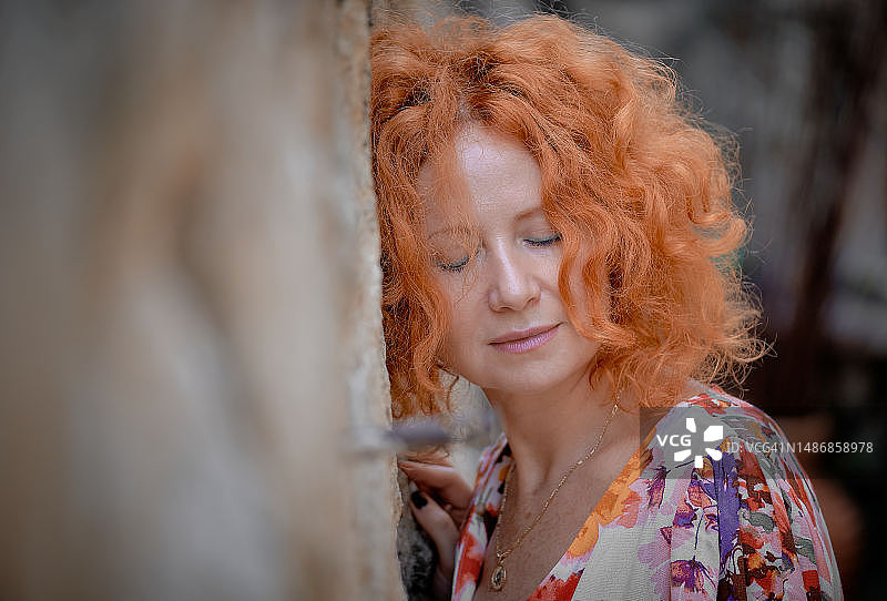 闭着眼睛将红色头发靠在墙上的女人特写图片素材