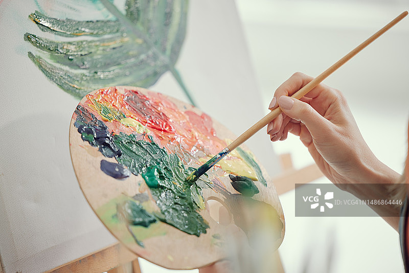 在客厅里，手和女人用画架在画布上进行艺术创作，享受艺术自由、爱好或活动。创意画家正在创作一幅色彩鲜艳的艺术图片，特写镜头图片素材