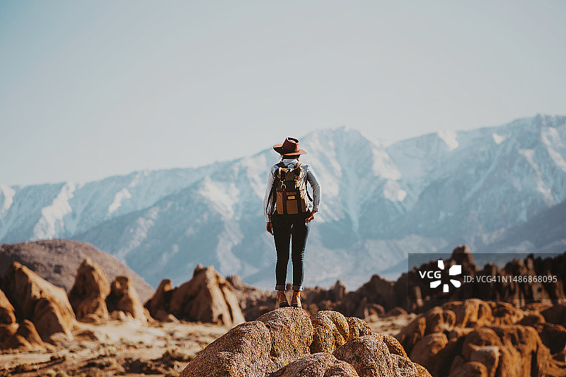 年轻女子背着旅行背包站在岩石上，背景是山脉的背影图片素材