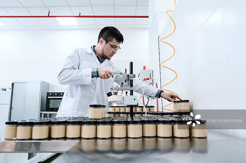 工厂工人用吸尘器清洁玻璃罐中的成品图片素材