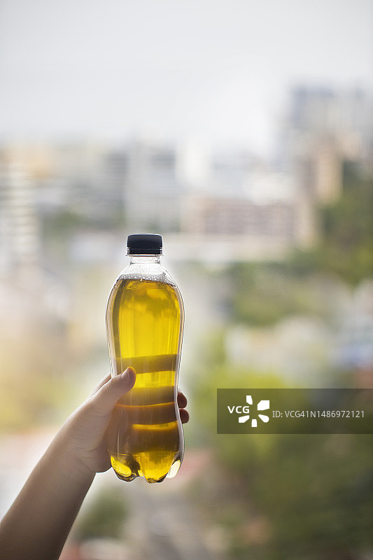 手持模糊天际线城市背景上的塑料驾驶瓶图片素材