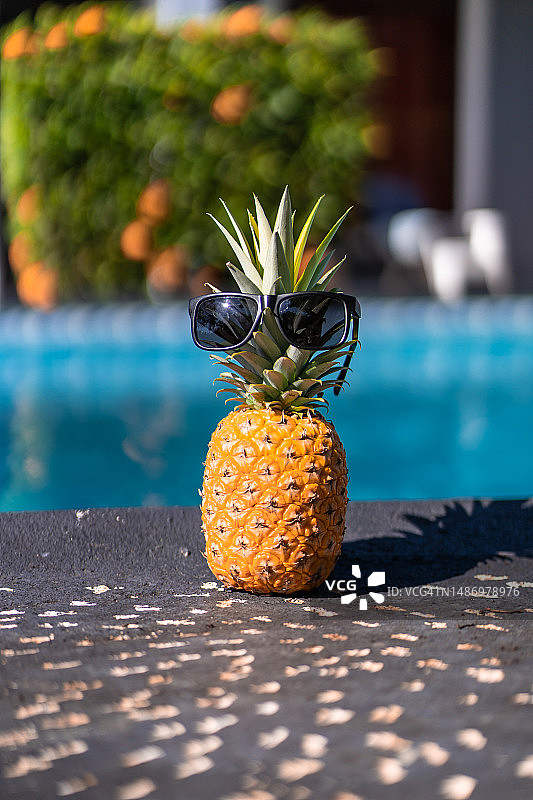 戴着太阳镜的菠萝在泳池里的竖版照片图片素材